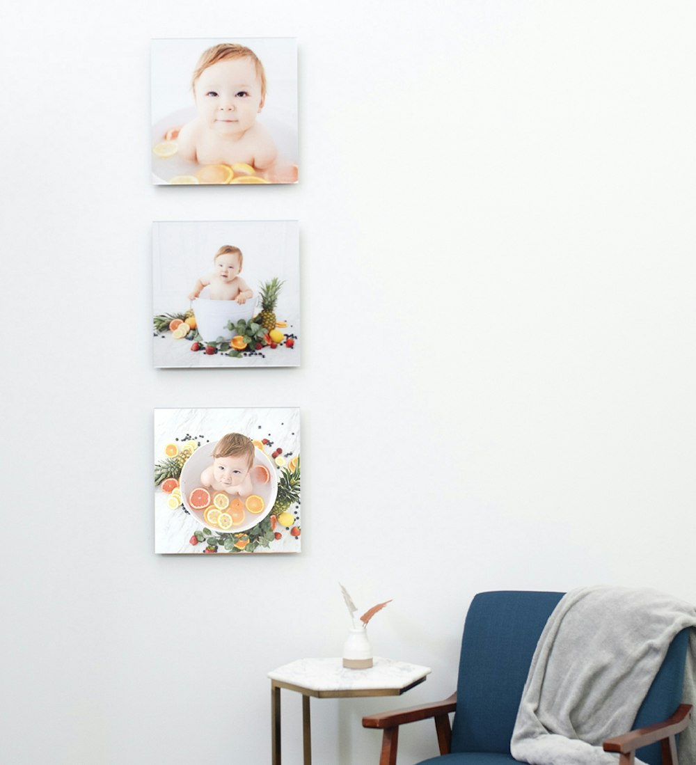 Three newborn portrait acrylic prints hung vertically by blue chair