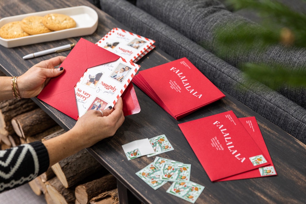 Holiday cards being placed in red printed envelopes on table with stamps