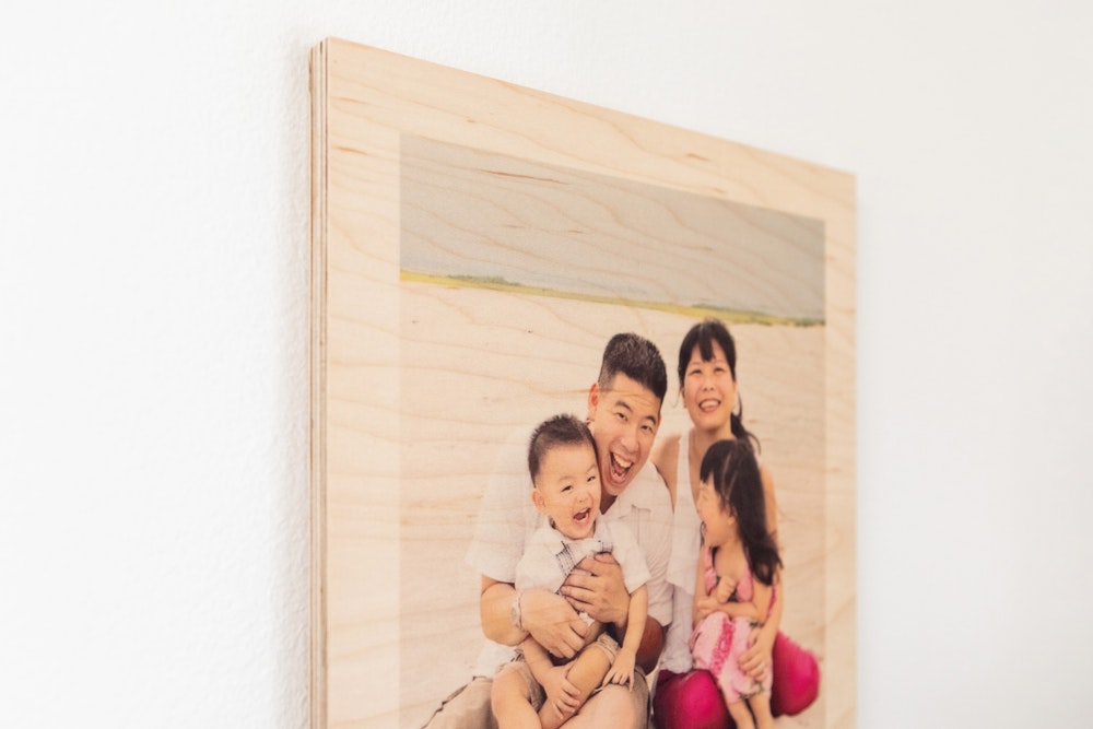 Close-up detail of Wood Print with border featuring a portrait of a family of four smiling and laughing, seated on the beach.