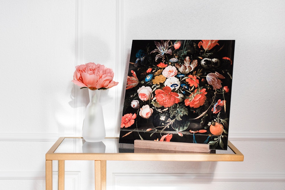 Vibrant floral artwork displayed on an walnut Wood Display Stand on a small table, paired with a single pink flower in a white vase beside it, against a white wall background.