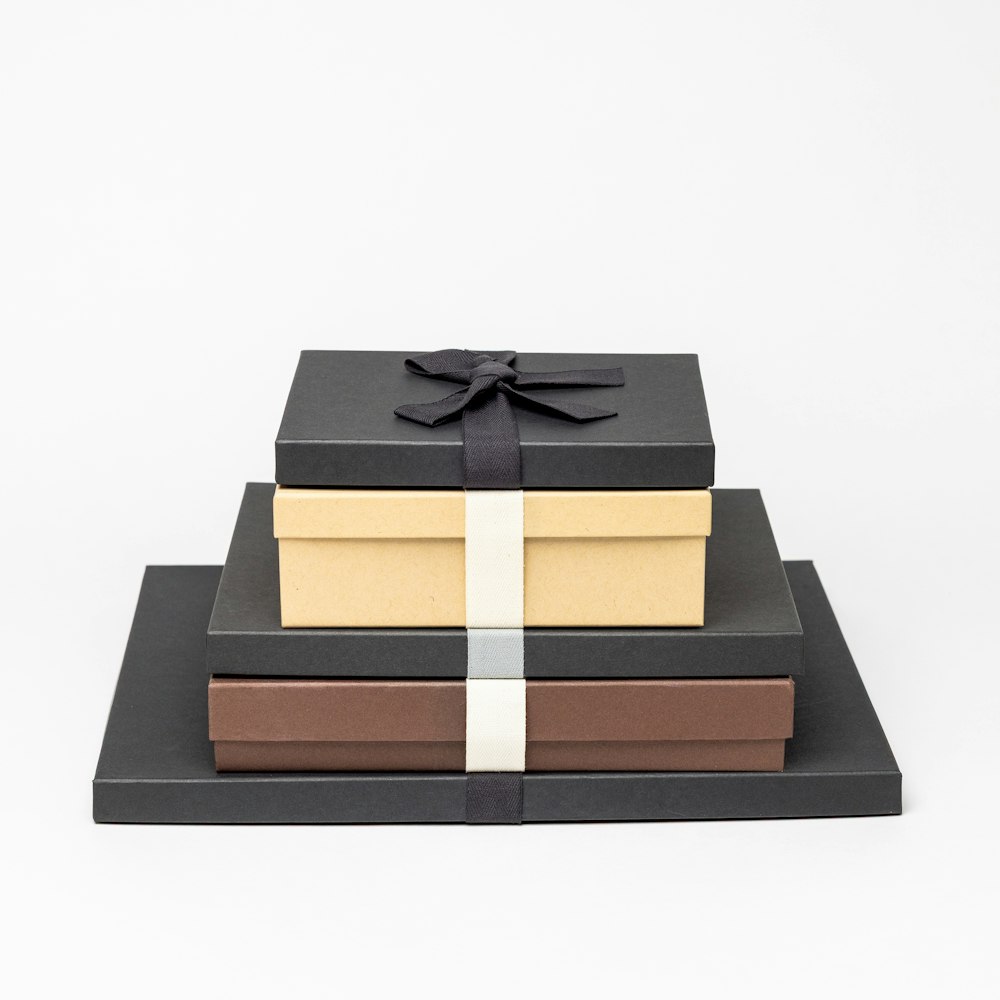 Multiple Premium Packaging boxes in several sizes, stacked from largest to smallest, with a few color options, such as Charcoal with Black Ribbon, Kraft with Cream Ribbon, and Brown with Cream Ribbon.
