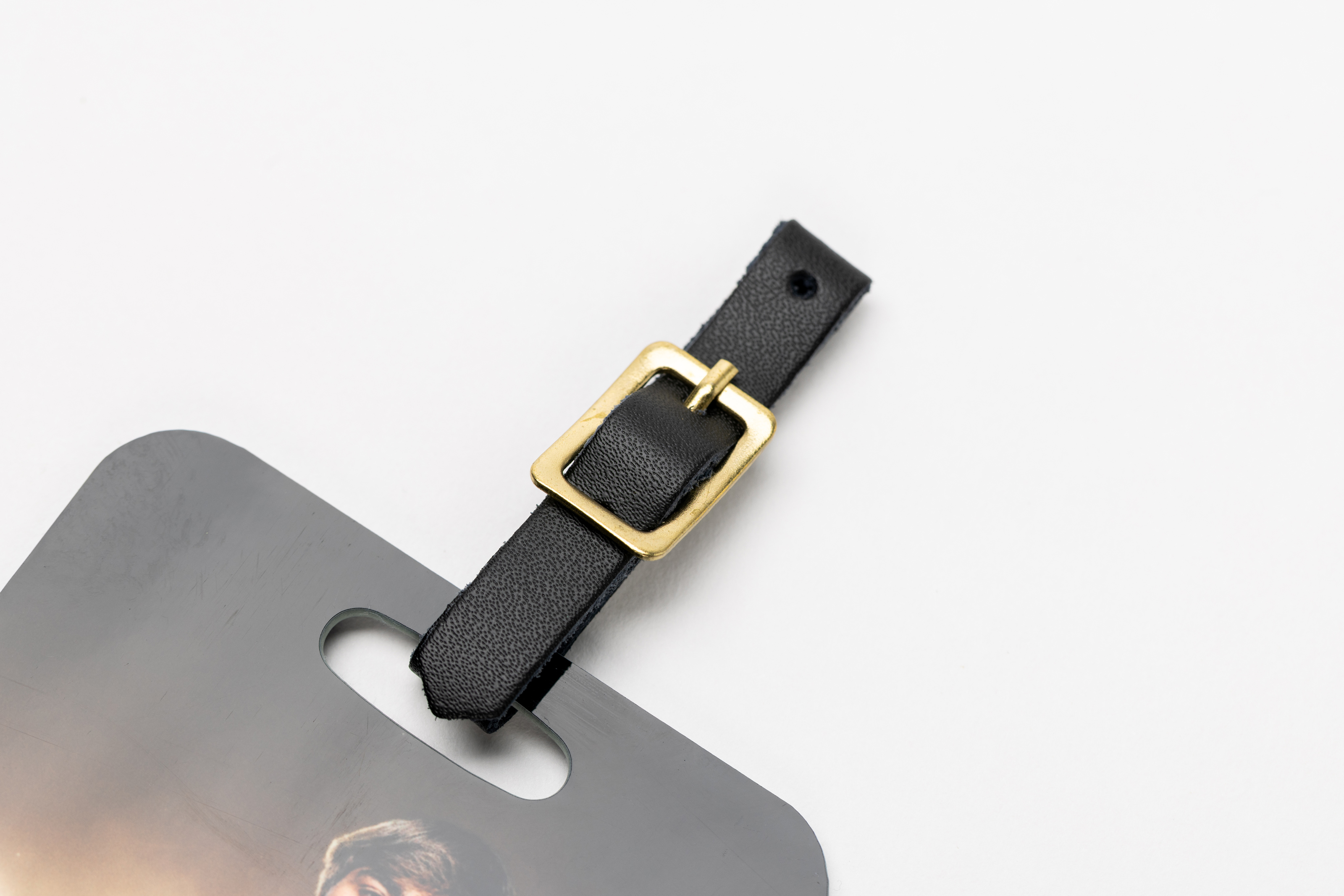 Close-up of black leather strap with gold clasp on Bag Tag over white background