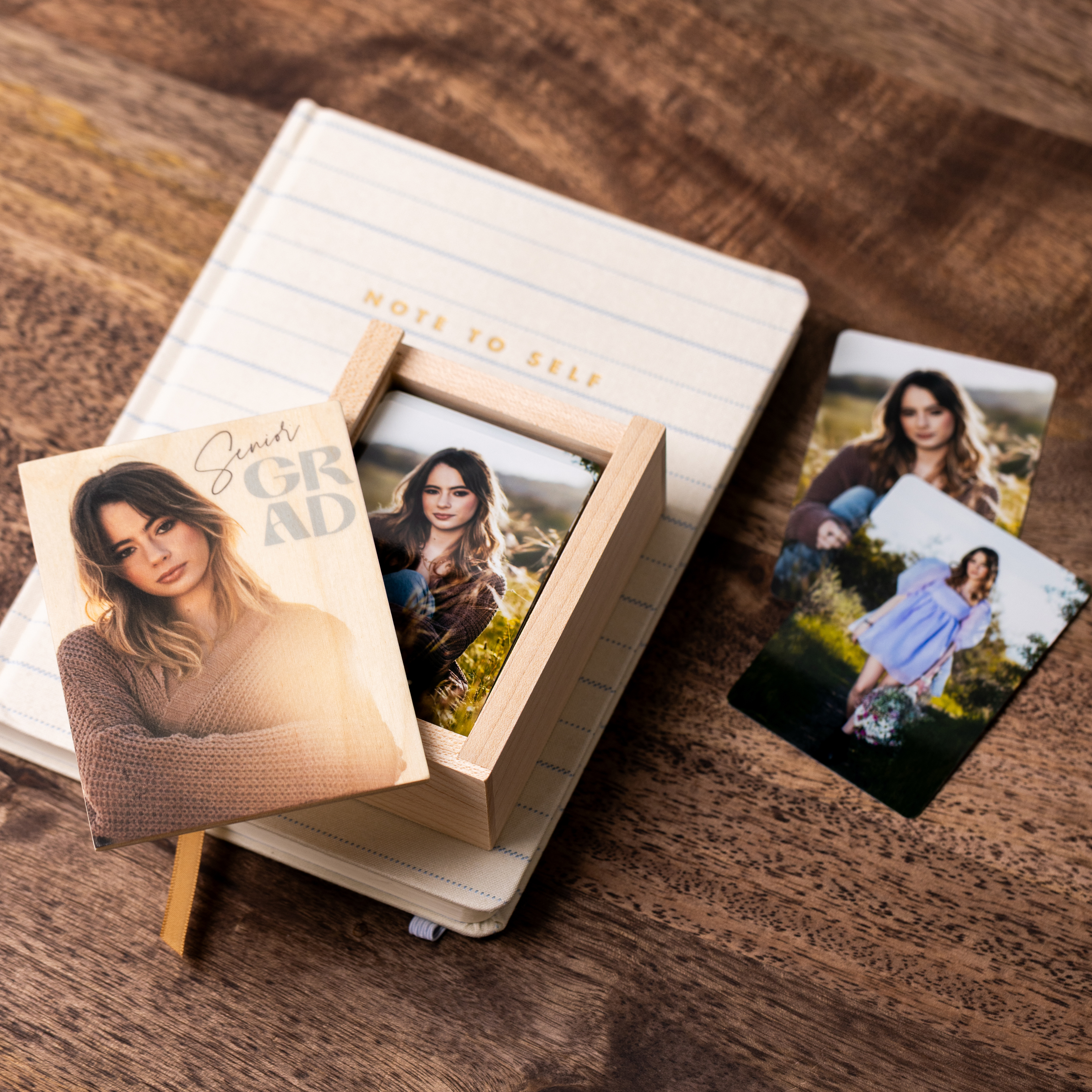 Senior portrait wallets next to and stored in a wallet-sized Wood Box on a small lined notesbook on a walnut wood tabletop