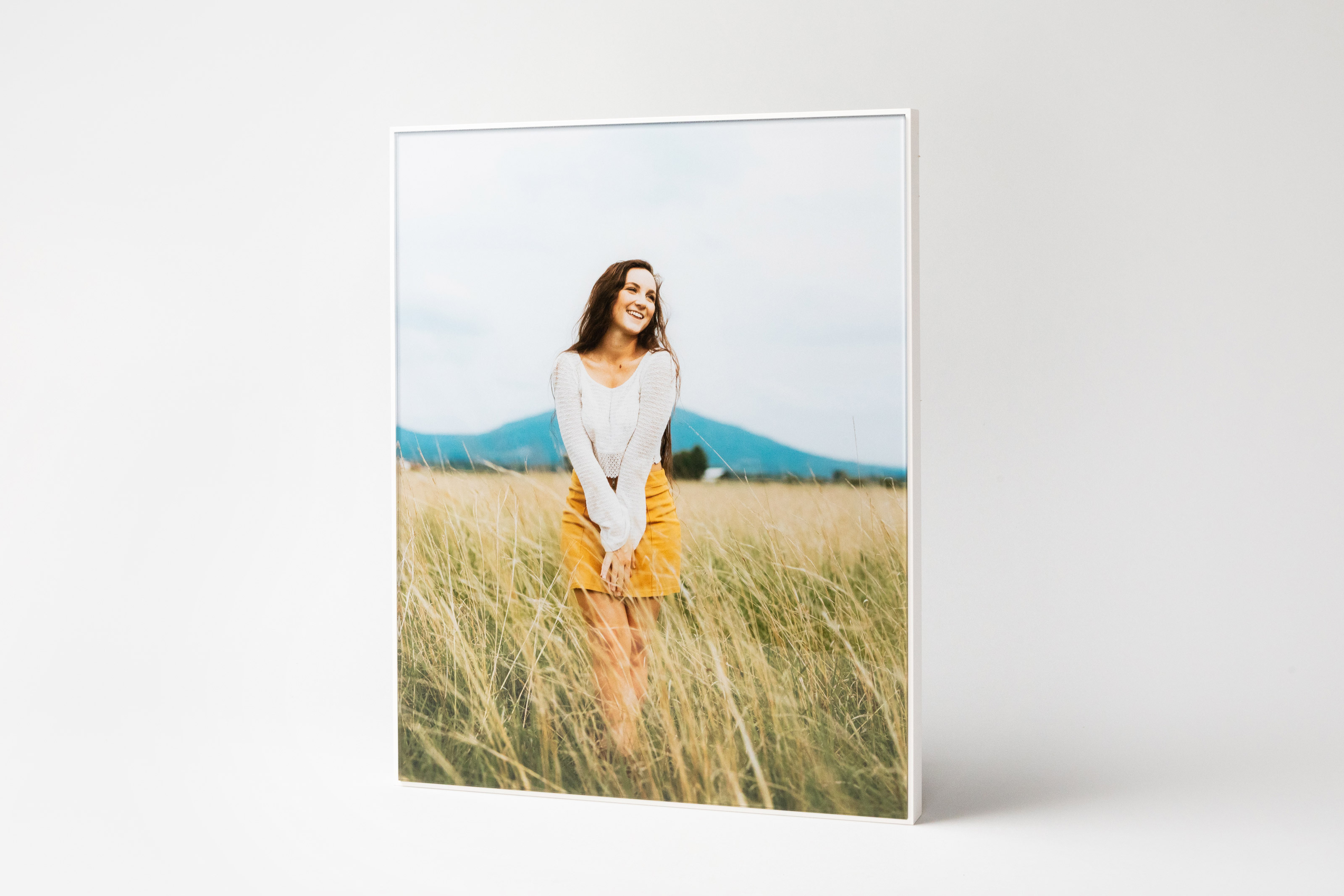 Senior portrait of a girl in a field displayed in a White Framed Acrylic Print standing on soft gray background