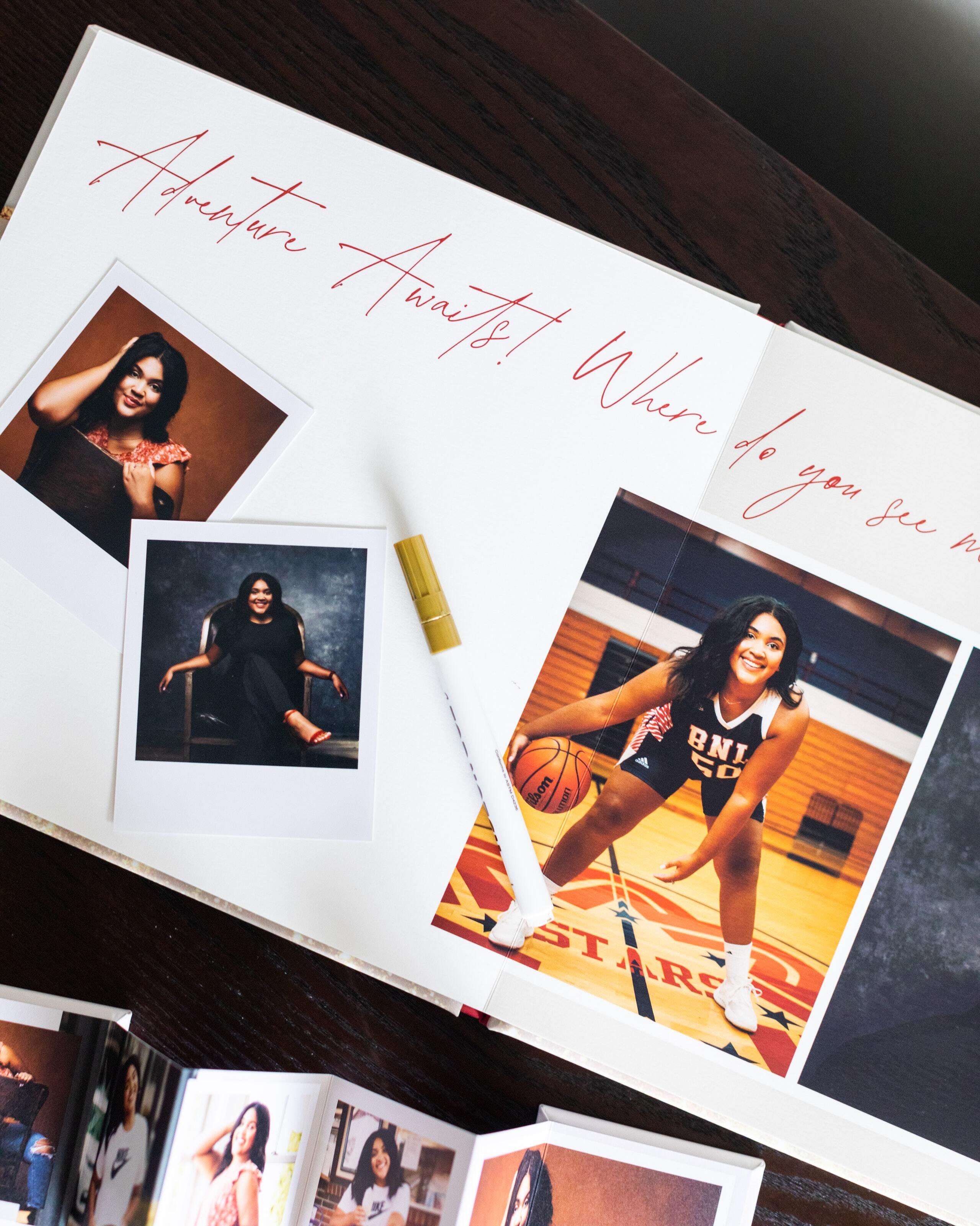 Open Layflat Book spread with red script lettering and a printed senior portrait, shown with loose prints and a signing pen.