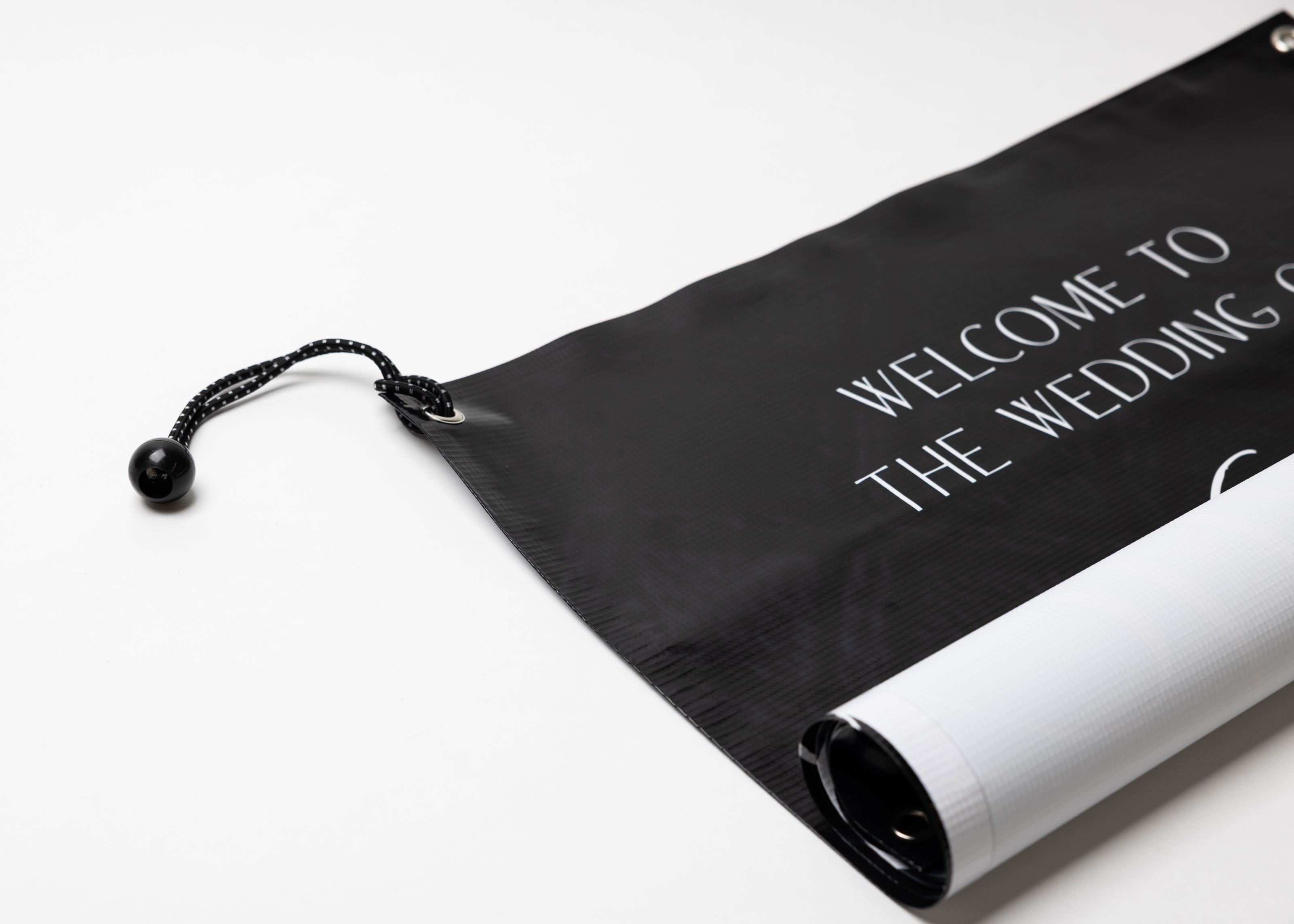 Bungees connected to silver grommets on a vertical vinyl banner printed with a messsage welcoming guests to a wedding