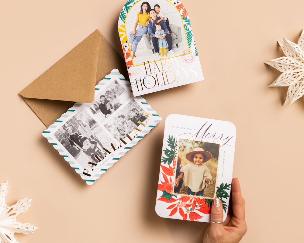 Hand holding foil-pressed holiday card over card and envelope styled flatlay
