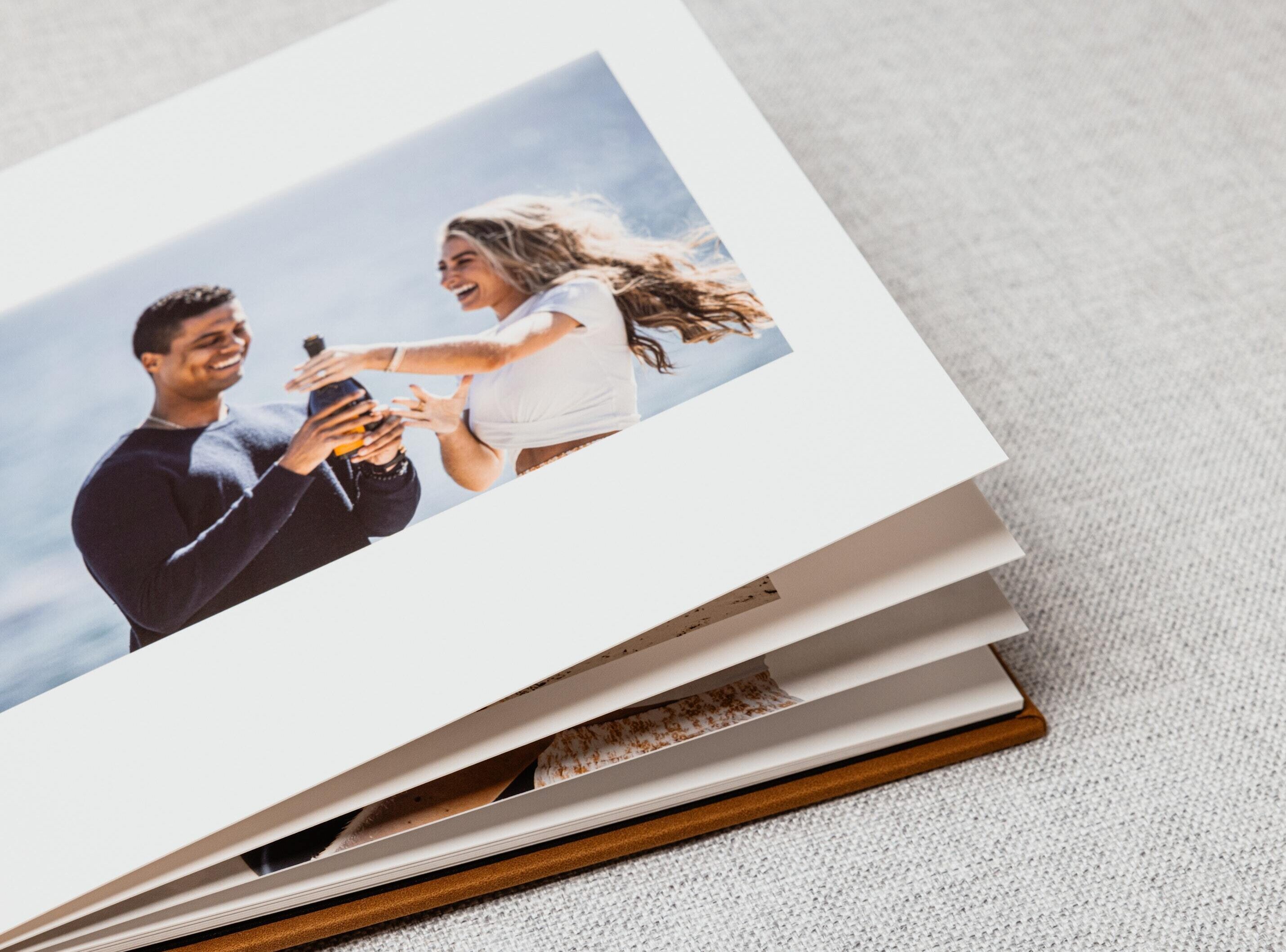 Close-up of an open layflat book’s thick pages lying completely flat, showing a full-bleed engagement photo across the spread.