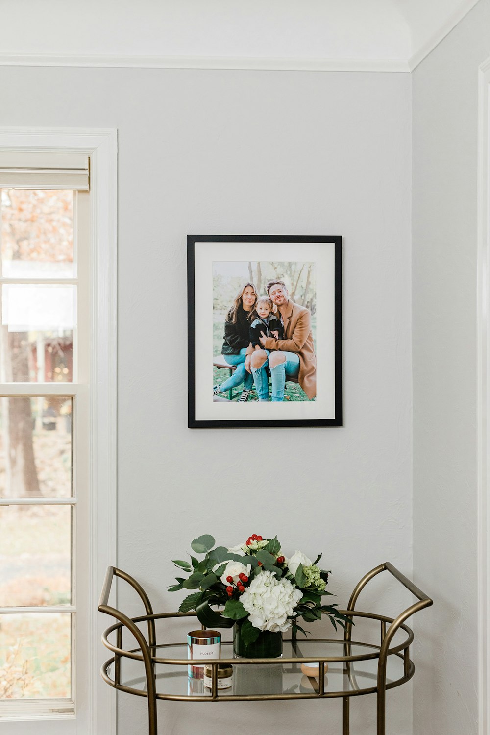 Family portrait in black framed print with mat hanging on wall by window