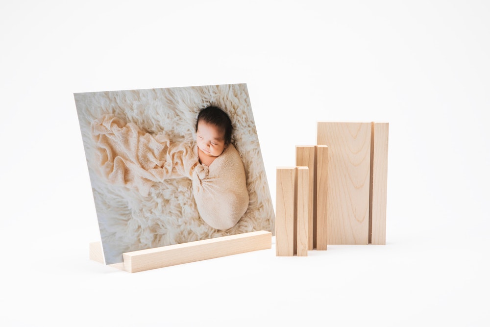 A mounted photo print of a sleeping baby on a maple Wood Display Stand next to a set of three stand size options on a plain white background.